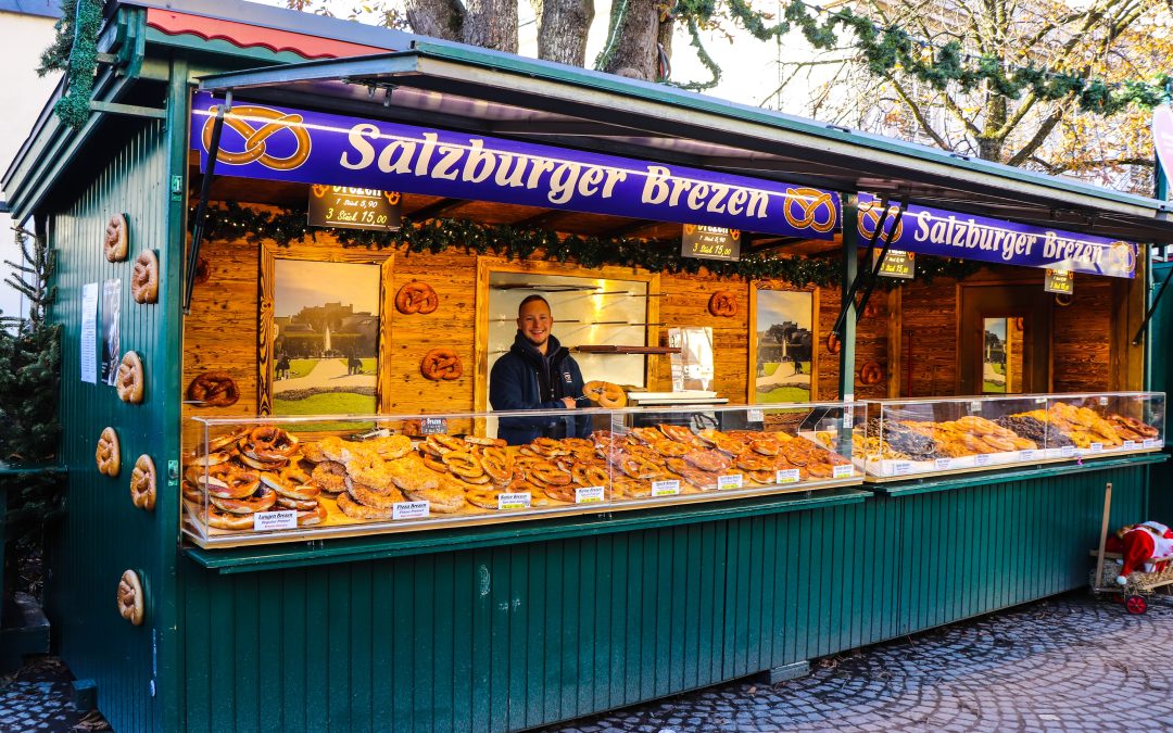 米拉贝尔广场上 Alexander Reisinger 的 Salzburger Brezen 小木屋，摊主站在摆着碱水结和甜味椒盐卷饼的玻璃柜后