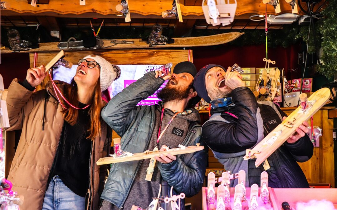 萨尔茨堡米拉贝尔广场圣诞市集 Apres Allstars 摊位前，三个人一起用 Shotski 喝酒