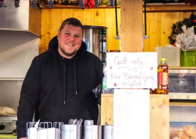 Lächelnder Standler hinter der Theke der Hütte der Familie Rettenbacher am Weihnachtsmarkt Mirabellplatz