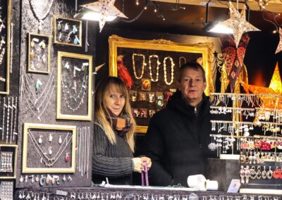 Standlerin und Standler in der Schmuckhütte von Markus Germayer zwischen gerahmten Ketten am Weihnachtsmarkt Mirabellplatz