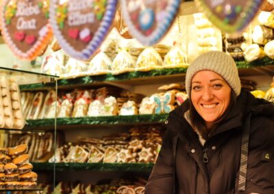Lächelnde Standlerin mit Wollmütze vor Regalen voller Lebkuchen in der Hütte von Susanne Meixner