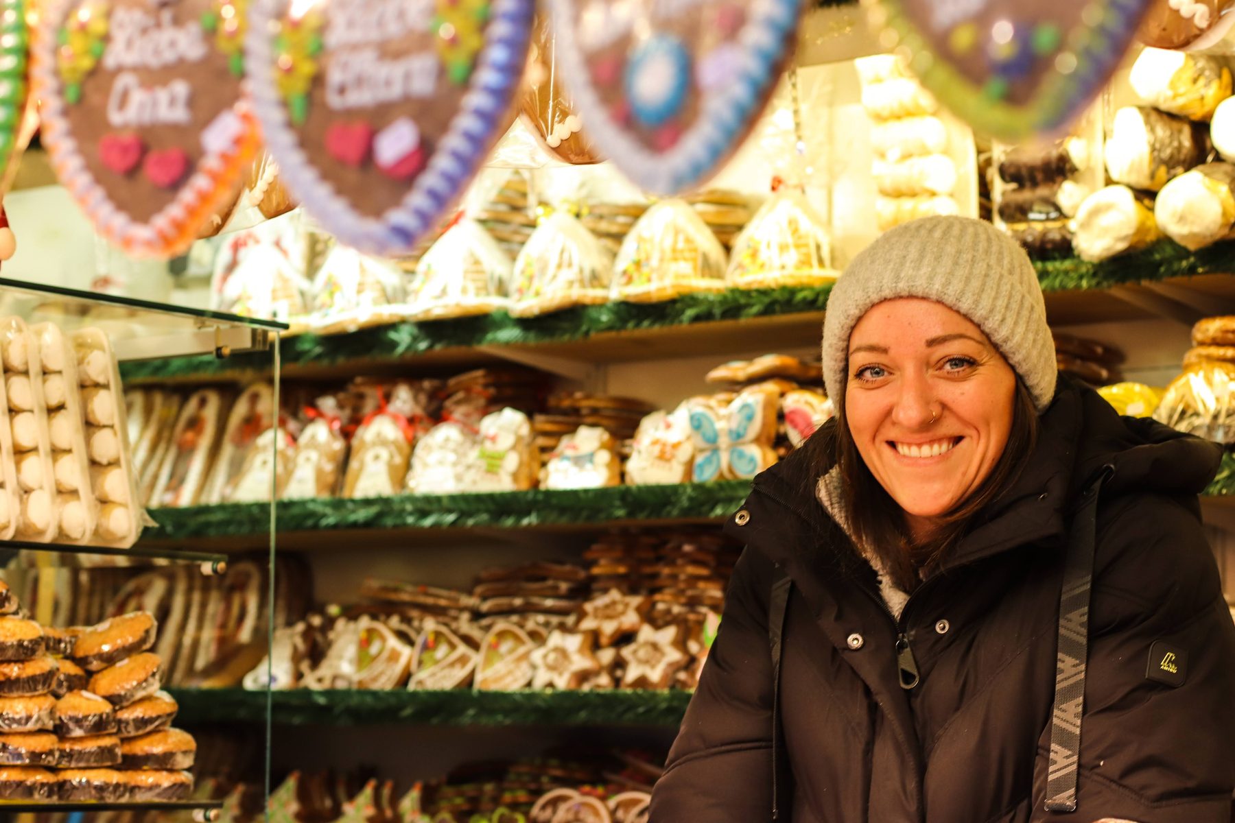 Susanne Meixnerのヒュッテで、Lebkuchenがいっぱいの棚の前でほほえむニット帽の店員