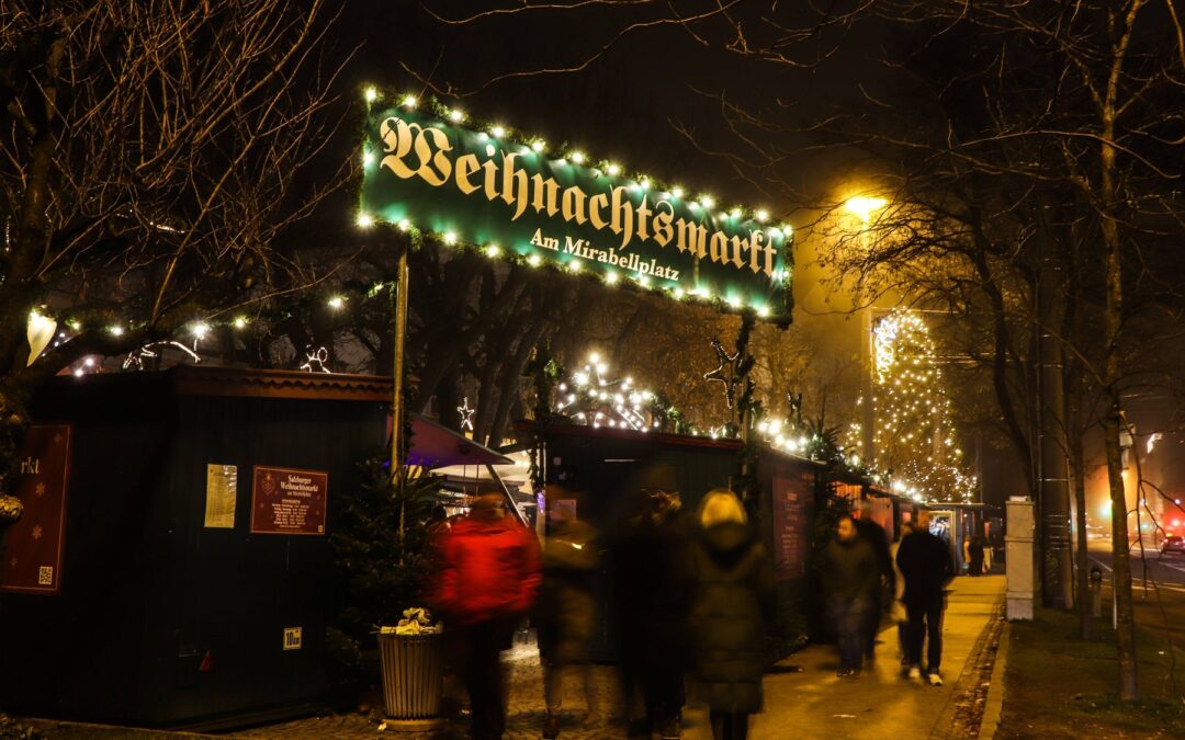 Beleuchteter Eingang zum Weihnachtsmarkt am Mirabellplatz in Salzburg am Abend mit Besuchern